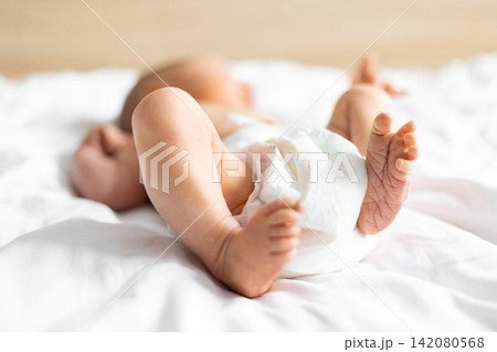 Close-up of a Caucasian newborn baby's tiny feet and legs, wearing a diaper and lying on soft white sheets Close-up of a Caucasian newborn baby's tiny feet and legs, wearing a diaper and lying on soft white sheets 142080568