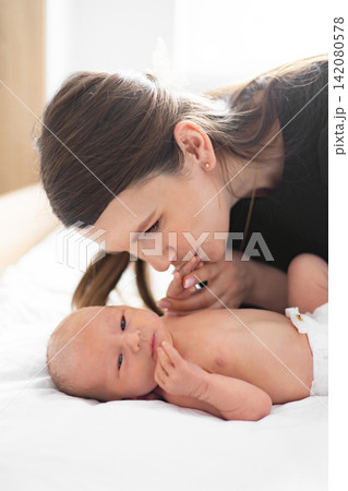 A tender moment captured as a mother gently kisses the hand of her newborn baby lying on a white surface A tender moment captured as a mother gently kisses the hand of her newborn baby lying on a white surface 142080578
