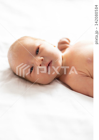 A close-up, soft-focus portrait of a newborn baby with light skin and dark eyes, resting on a white textured surface 142080584