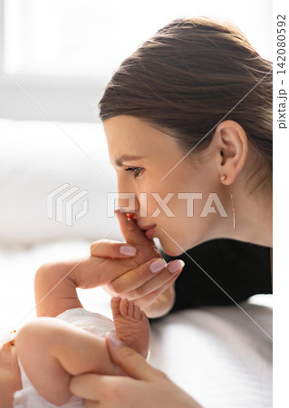 A tender moment captured as a mother gently kisses her newborn baby's tiny foot, showcasing maternal love and connection A tender moment captured as a mother gently kisses her newborn baby's tiny foot, showcasing maternal love and connection 142080592