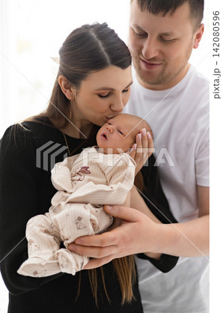 A tender moment captured as a mother kisses her newborn baby while the father looks on lovingly A tender moment captured as a mother kisses her newborn baby while the father looks on lovingly 142080596