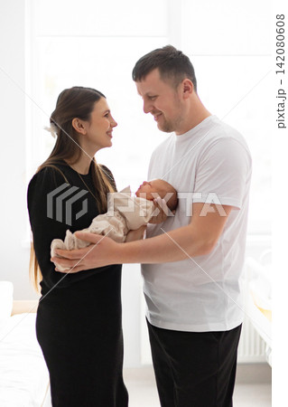 A happy family of three, a mother and father holding their newborn baby, sharing a tender moment together A happy family of three, a mother and father holding their newborn baby, sharing a tender moment together 142080608