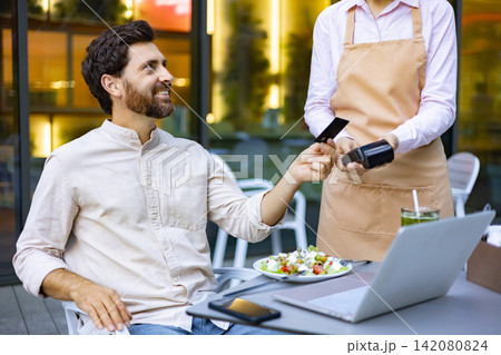 A man smiles while paying for his meal at an outdoor cafe using a credit card and a portable payment terminal A man smiles while paying for his meal at an outdoor cafe using a credit card and a portable payment terminal 142080824
