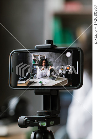 A woman is recording a video of herself using a smartphone mounted on a tripod, engaging with her audience A woman is recording a video of herself using a smartphone mounted on a tripod, engaging with her audience 142080957