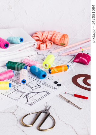 Sewing patterns, threads, scissors, templates and needles on a work table vertical view Sewing patterns, threads, scissors, templates and needles on a work table vertical view 142081094