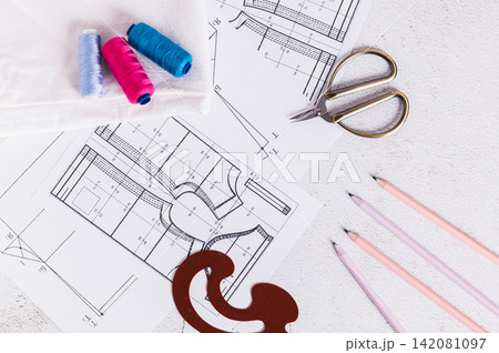 Close up of sewing patterns, threads, scissors, templates and needles on a work table top view 142081097
