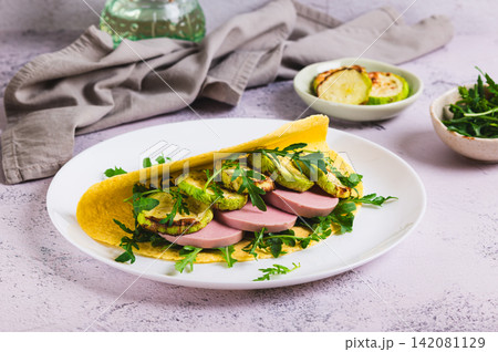 Tortilla with baked zucchini, sausage and arugula on a plate on the table Tortilla with baked zucchini, sausage and arugula on a plate on the table 142081129