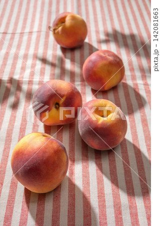 Fresh Ripe Peaches on Red Striped Tablecloth in Sunny Light Fresh Ripe Peaches on Red Striped Tablecloth in Sunny Light 142081663