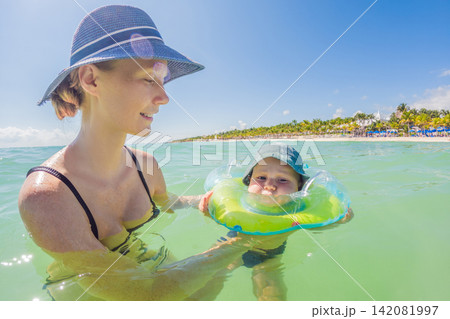 Woman and baby spending time by the Caribbean shore in Mexico, enjoying warm turquoise water, beach vacation, motherhood and travel with baby concept Woman and baby spending time by the Caribbean shore in Mexico, enjoying warm turquoise water, beach vacation, motherhood and travel with baby concept 142081997