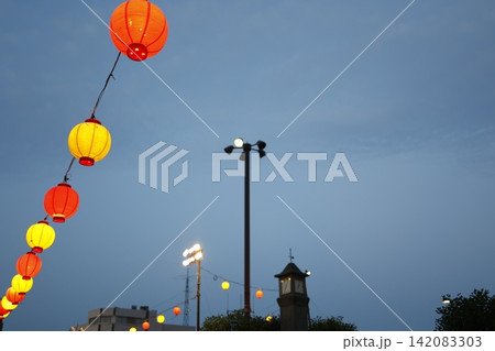 夕刻の曇り空に灯る祭り提灯。赤黄の装飾ランプと街灯。夜間イベント 夕刻の曇り空に灯る祭り提灯。赤黄の装飾ランプと街灯。夜間イベント 142083303