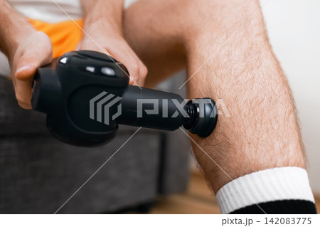 Close-up of a person using a percussion massage gun on their leg muscle for post-workout recovery, myofascial release, and to ease muscle tension. 142083775