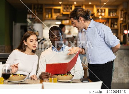 Man waiter communicates with multiethnic friends customers, answers questions 142084348