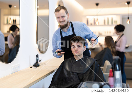 Young male hairdresser giving haircut to young guy Young male hairdresser giving haircut to young guy 142084420