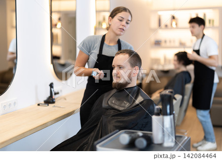 Young female hairdresser giving haircut to young man 142084464