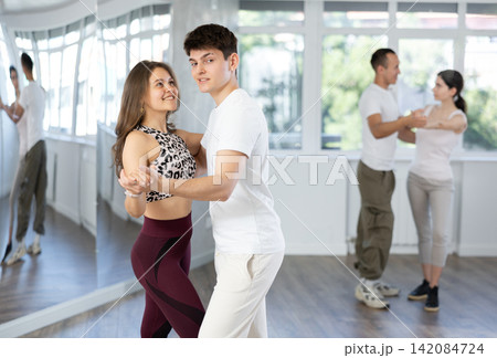 Pretty young woman dancing waltz with partner at group of multinational people in ballroom dancing class Pretty young woman dancing waltz with partner at group of multinational people in ballroom dancing class 142084724