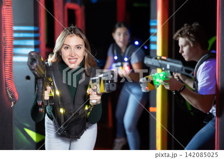 Joyous girl with laser pistol playing laser tag with friends on labyrinth 142085025