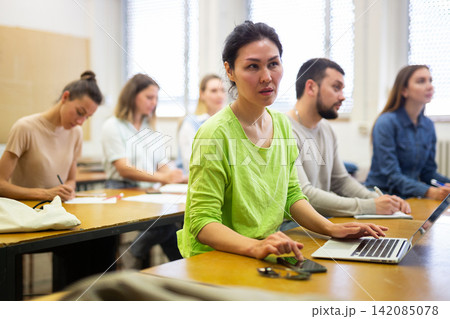 Smart female studying in classroom, listening to lecturer and writing in notebook and laptop 142085078