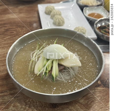 Authentic Pyongyang naengmyeon with chewy buckwheat noodles in cold, clear broth, offering a refreshing and delicate flavor. Perfect for traditional Korean cuisine menus and summer dishes. Authentic Pyongyang naengmyeon with chewy buckwheat noodles in cold, clear broth, offering a refreshing and delicate flavor. Perfect for traditional Korean cuisine menus and summer dishes. 142085654