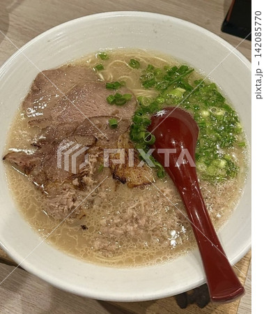 A steaming bowl of ramen with curly noodles, sliced chashu pork, a soft-boiled egg, and green onions in a rich, savory broth. An inviting Japanese comfort food scene. A steaming bowl of ramen with curly noodles, sliced chashu pork, a soft-boiled egg, and green onions in a rich, savory broth. An inviting Japanese comfort food scene. 142085770