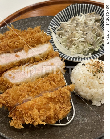 Crispy tonkatsu, a Japanese-style breaded and deep-fried pork cutlet, served with shredded cabbage and drizzled with savory sauce. A delightful balance of crunchy texture and juicy meat. 142085780