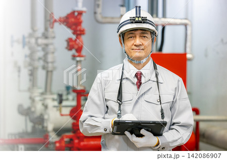 ボイラー室でタブレットを使って設備点検をするシニア男性作業員 ボイラー室でタブレットを使って設備点検をするシニア男性作業員 142086907