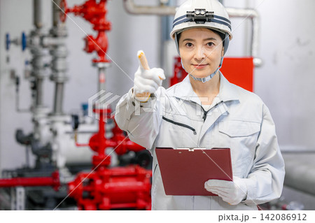 ボイラー室でタブレットを使って設備点検をする女性作業員 ボイラー室でタブレットを使って設備点検をする女性作業員 142086912