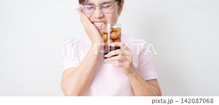 Woman drinking carbonated ice water and feeling sensitive teeth to cold pain, hand holding glass of cold sparkling water. dental health problem from soda acidity, toothache and oral care concept 142087068