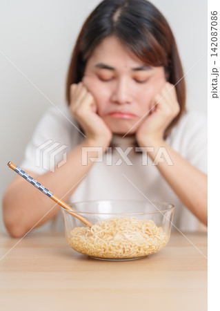 Bored young Asian woman eating instant noodles at home. Exhausted female looking unhappy while eating bowl ramen. quick meal after work, burnout and unhealthy eating habit, lifestyle and cheap meal Bored young Asian woman eating instant noodles at home. Exhausted female looking unhappy while eating bowl ramen. quick meal after work, burnout and unhealthy eating habit, lifestyle and cheap meal 142087086