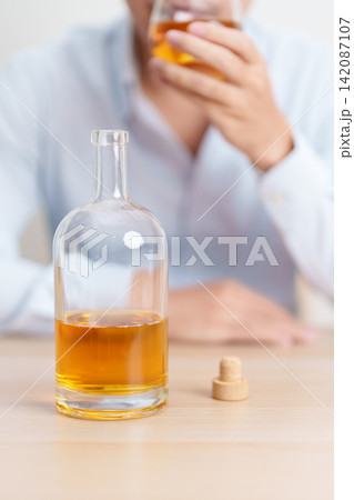 Stressed man drinking whiskey alone with problem. Exhausted drunk man looking stressed and sleepy. Alcohol addiction, Alcoholism, emotional distress and mental health concept 142087107