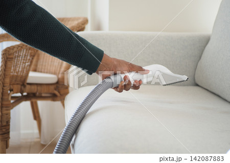 Cleaning a couch with a vacuum hose in a living room 142087883
