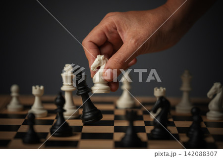 hand holding white chess knight taking black king, strategy concept hand holding white chess knight taking black king, strategy concept 142088307