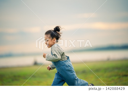happy preschool child girl running on a grass field near river happy preschool child girl running on a grass field near river 142088429
