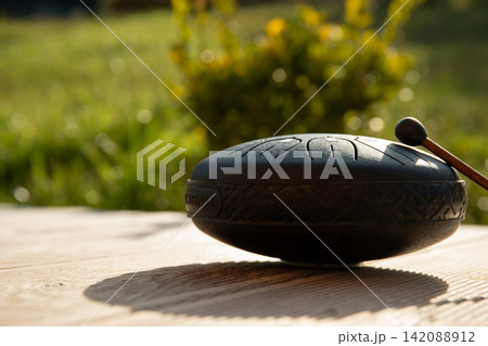 Tbilisi, Georgia - October 10, 2025: Handpan shines under sunlight on rustic table Tbilisi, Georgia - October 10, 2025: Handpan shines under sunlight on rustic table 142088912