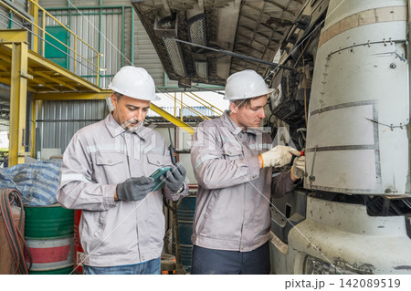 Two mechanics repairing a truck engine in an industrial workshop. 142089519
