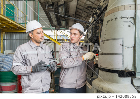Two mechanics repairing a truck engine in an industrial workshop. 142089558