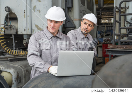 Two mechanics discussing maintenance on laptop at industrial workshop. Two mechanics discussing maintenance on laptop at industrial workshop. 142089644