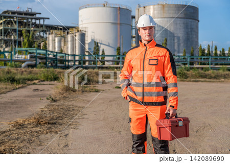 Construction worker in safety gear holding toolbox at industrial site Construction worker in safety gear holding toolbox at industrial site 142089690