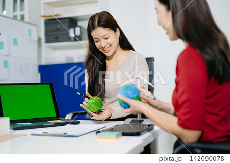 Two smiling female architects collaborate on sustainable eco project models with solar panels and wind turbine in office. Green renewable energy Two smiling female architects collaborate on sustainable eco project models with solar panels and wind turbine in office. Green renewable energy 142090078