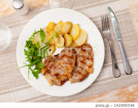 Fried pork served with potatoes and arugula Fried pork served with potatoes and arugula 142090546