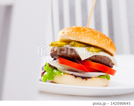Cheeseburger. Appetizing cheeseburger with grilled beef patty, fresh vegetables and pickled cucumbers.. 142090645