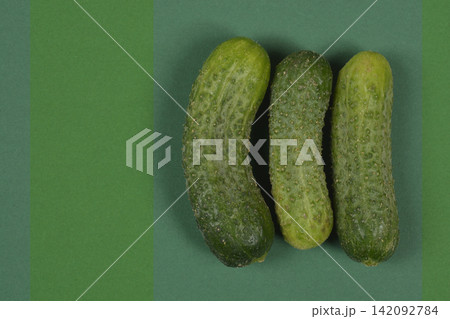 Three green gherkin cucumbers on green striped background Three green gherkin cucumbers on green striped background 142092784