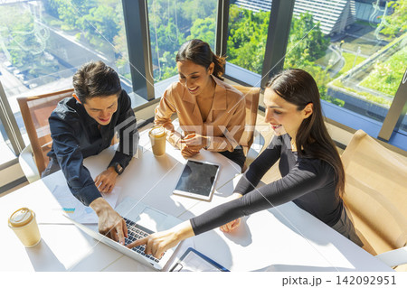 Caucasian businesswoman pointing to laptop screen while talking to her Asian coworker in office of a multinational company. Discussing work. Caucasian businesswoman pointing to laptop screen while talking to her Asian coworker in office of a multinational company. Discussing work. 142092951
