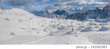 Ski mountaineer standing on a snowy rock in the Dolomites with wind blowing snow across alpine slopes, capturing winter adventure, solitude and dramatic mountain landscape. Ski mountaineer standing on a snowy rock in the Dolomites with wind blowing snow across alpine slopes, capturing winter adventure, solitude and dramatic mountain landscape. 142092963