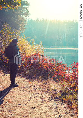 Man tourist stands on a picturesque lakeshore in the autumn morning and looking at the sunrise Man tourist stands on a picturesque lakeshore in the autumn morning and looking at the sunrise 142093183
