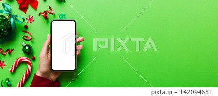 christmas mockup with space for text. christmas advertising, app template. hand holding phone with empty screen on table background. Happy New Year and Xmas Flat lay 142094681