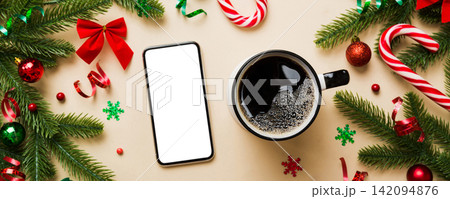 top view of smart phone with hot cup of coffee. Christmas decoration on colored background top view of smart phone with hot cup of coffee. Christmas decoration on colored background 142094876