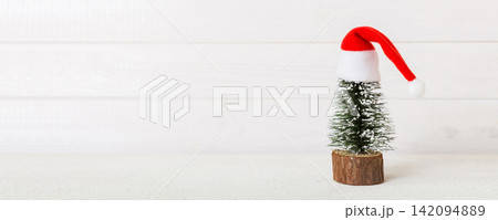 One small Christmas tree with santa hat on colored background. new year decoration with copy space One small Christmas tree with santa hat on colored background. new year decoration with copy space 142094889