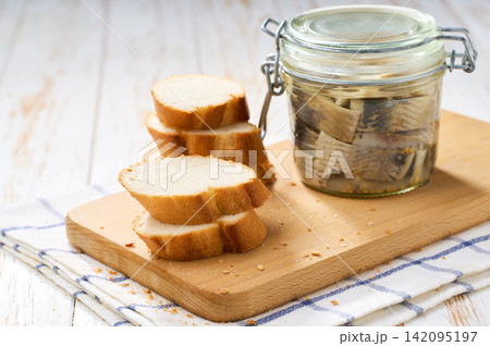 Marinated herring in a jar with herbs on a white table, selective focus. Herring marinated with oil and salt Marinated herring in a jar with herbs on a white table, selective focus. Herring marinated with oil and salt 142095197