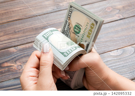 Perspective view of female hands counting money. One hundred dollar banknotes on wooden background. Salary concept. Bribe concept Perspective view of female hands counting money. One hundred dollar banknotes on wooden background. Salary concept. Bribe concept 142095332