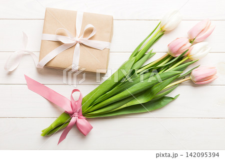 Pink tulips flowers and gift or present box on colored table background. Mothers Day, Birthday, Womens Day, celebration concept. Space for text top view Pink tulips flowers and gift or present box on colored table background. Mothers Day, Birthday, Womens Day, celebration concept. Space for text top view 142095394